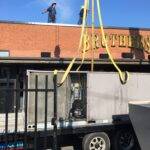 An old rooftop unit being set on trailer and hauled to recycling center