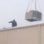 A rooftop unit being set on a roof in the winter