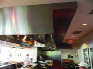 A commercial kitchen hood system above a chef preparing food