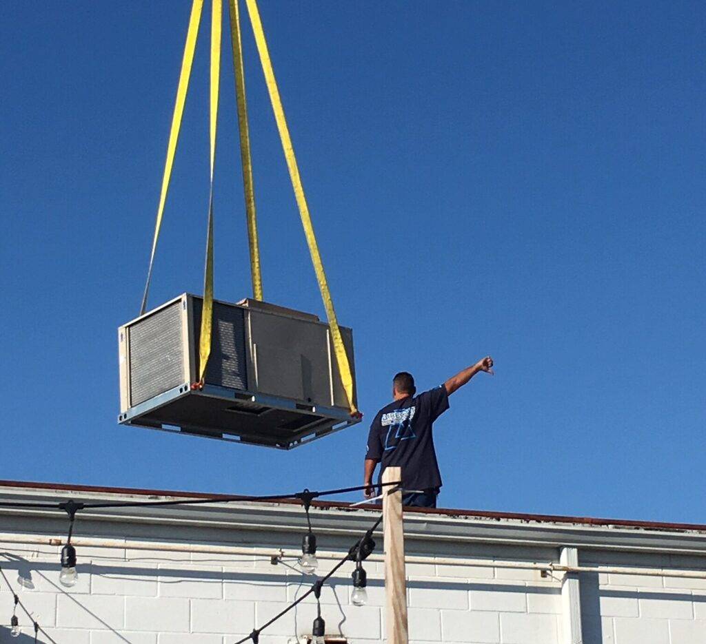 An AireCom installer directing a crane setting a rooftop unit